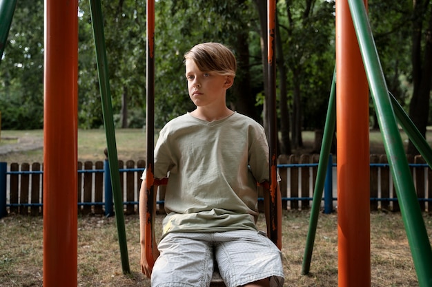 Front view sad boy sitting on swing