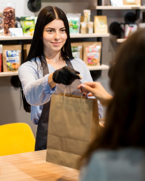 Front view sales assistant handing out groceries bag