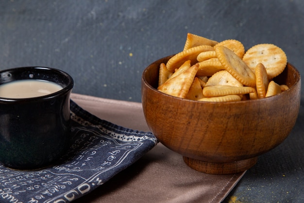 Front view salted crisps with black cup of milk on grey