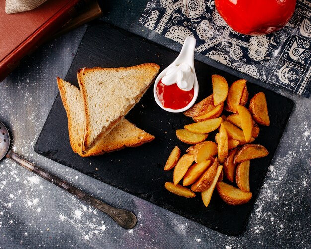 Front view sandwiches along with fried potatoes inside black plate on the grey floor