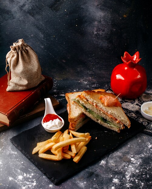 검은 책상과 회색 바닥에 감자 튀김과 함께 얇게 썬 전면보기 샌드위치
