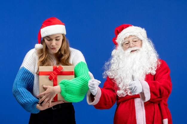 Front view of santa claus along with female who's holding present on a blue wall