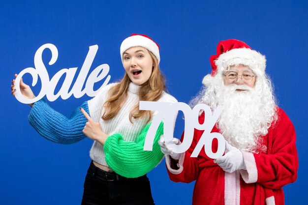 Front view of santa claus along with woman holding sale writings on blue wall