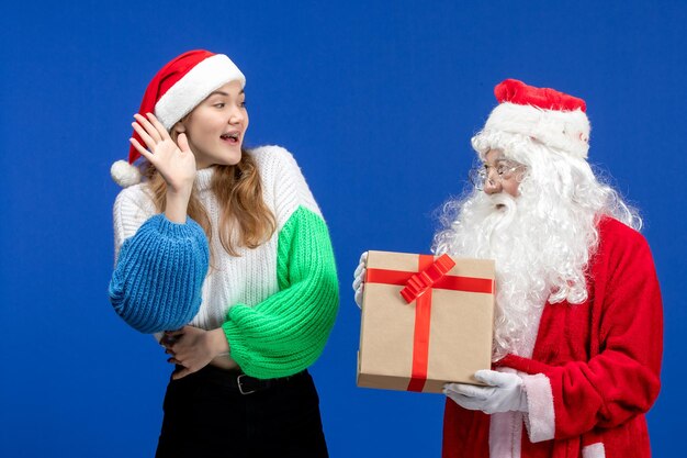 Front view of santa claus along with young female holding present on blue wall