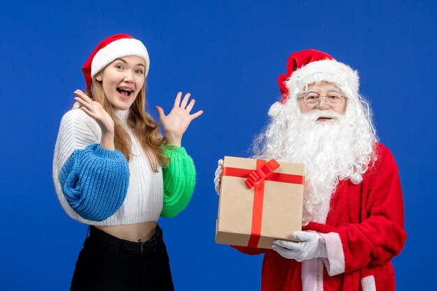 Front view of santa claus along with young female holding present on blue wall