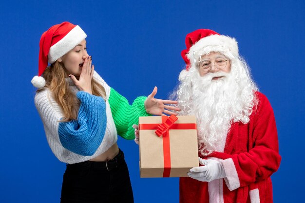 Front view of santa claus along with young female holding present on blue wall