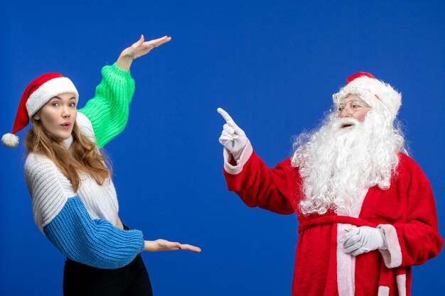 Вид спереди санта-клауса вместе с молодой женщиной, просто стоящей на синей модели новогодних праздников