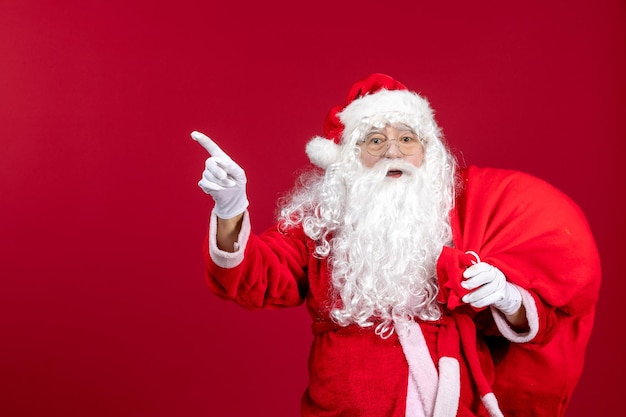 Front view santa claus carrying bag full of presents pointing on red emotion new year christmas holiday