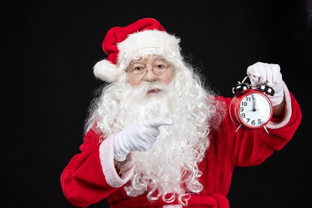Front view santa claus in classic red suit holding clocks