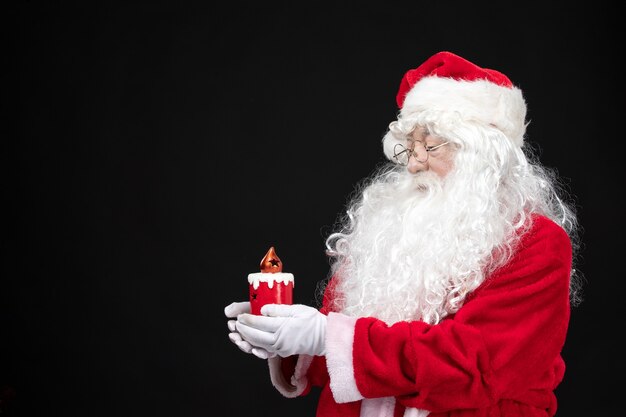 Front view santa claus in classic red suit holding holiday candle