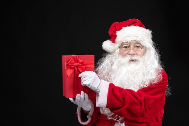 Free photo front view santa claus in classic red suit holding present