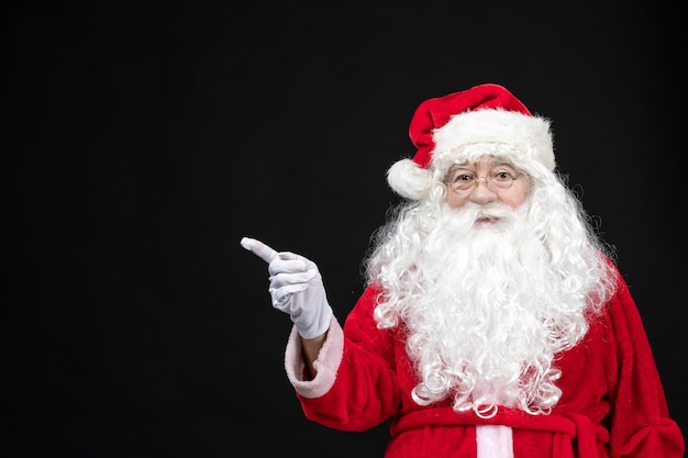 Front view of santa claus in classic red suit with white beard on black wall