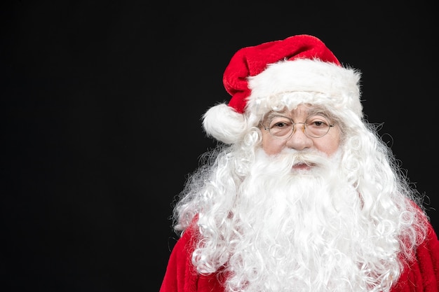 Front view of santa claus in classic red suit with white beard standing on black wall