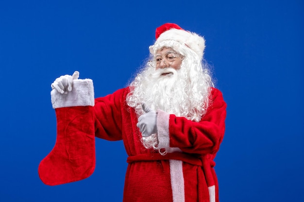 Front view santa claus holding big christmas sock on a blue color christmas snow