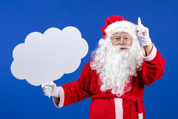 Free photo front view santa claus holding big cloud shaped sign on blue floor snow color christmas