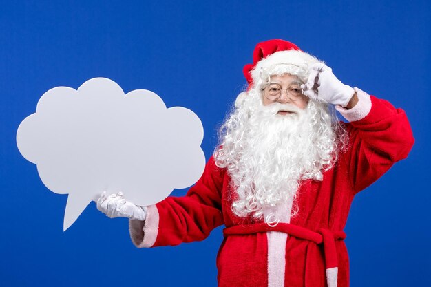 Front view santa claus holding big white cloud shaped sign on a blue color snow holiday christmas