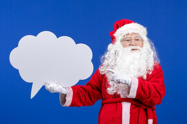 Front view santa claus holding big white cloud shaped sign on blue color snow holiday christmas