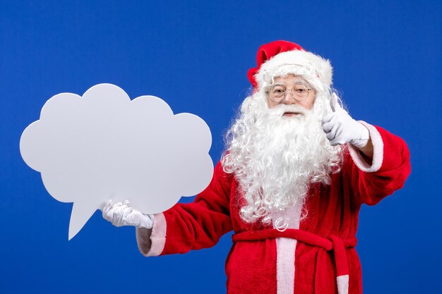 Front view santa claus holding big white cloud shaped sign on the blue color snow holiday christmas