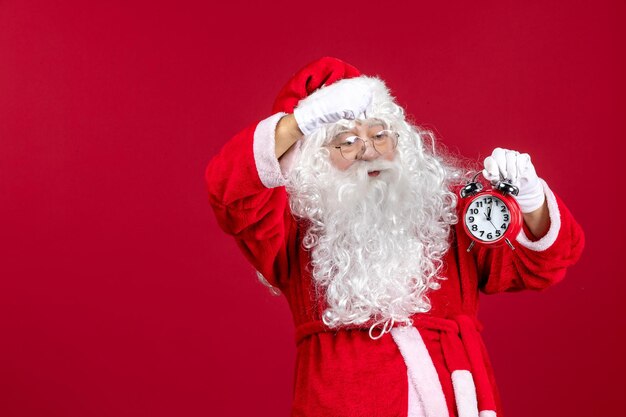 赤いクリスマスの休日の感情に時計を保持している正面のサンタクロース