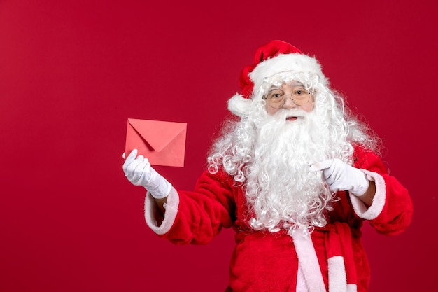 Vista frontale babbo natale che tiene busta con lettera di auguri da bambino su un'emozione rossa capodanno