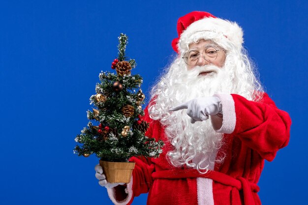 Front view santa claus holding little new year tree on a blue christmas new year