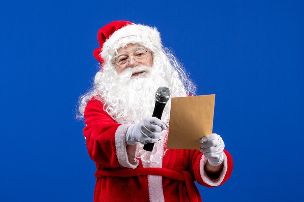 Front view santa claus holding mic and reading letter on blue new year color holiday christmas snow