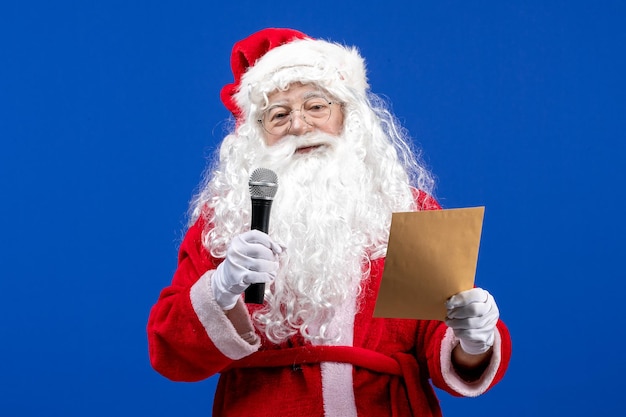 Front view santa claus holding mic and reading letter on the blue new year color holiday christmas snow