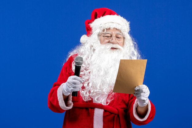 Front view santa claus holding mic and reading letter on blue new year color holiday xmas snow