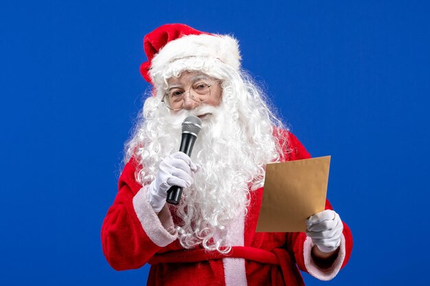 Front view santa claus holding mic and reading letter on blue new year color holidays christmas snow