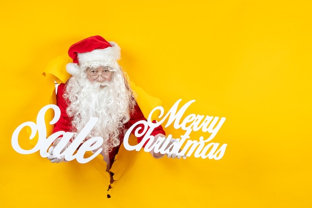 Бесплатное фото Вид спереди санта-клауса, держащего распродажу и веселых рождественских сочинений