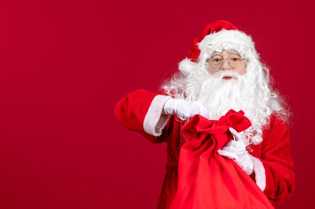 Vista frontale babbo natale che apre la borsa rossa piena di regali per i bambini in vacanza rossa emozione di natale