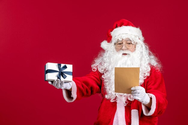 Front view santa claus reading letter from kid and holding present on a red emotion gift xmas holiday