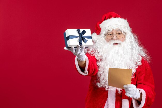 Front view santa claus reading letter from kid and holding present on red floor emotion gift xmas holiday