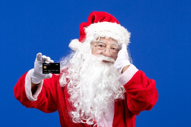 Front view santa claus in red clothes with white bear holding black bank card on a blue color holiday