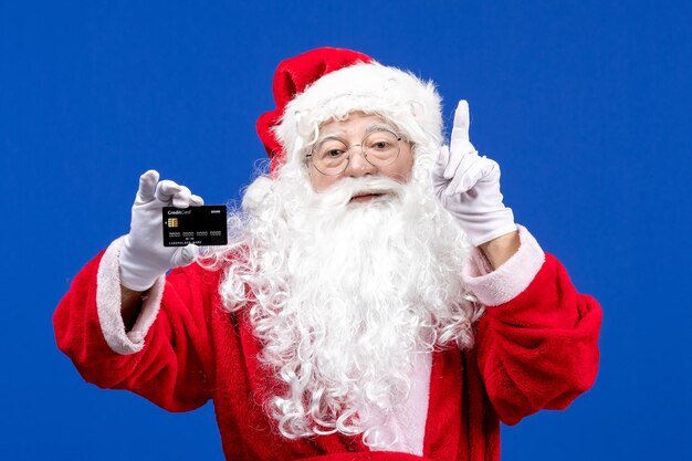 Front view santa claus in red clothes with white bear holding black bank card on blue color