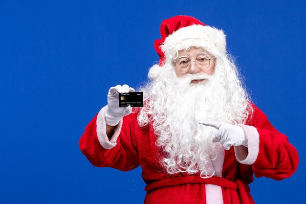 Front view santa claus in red suit holding bank card on a blue present xmas color new year holiday