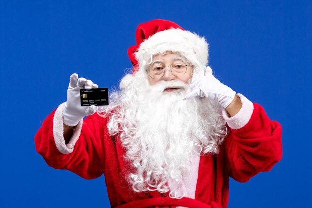 Front view santa claus in red suit holding black bank card on the blue color holiday present xmas