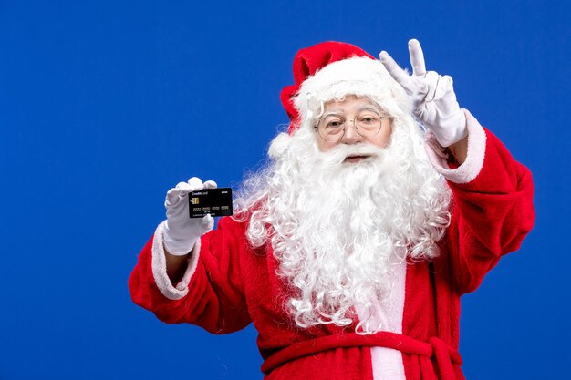 Front view santa claus in red suit holding black bank card on a blue present xmas color holiday