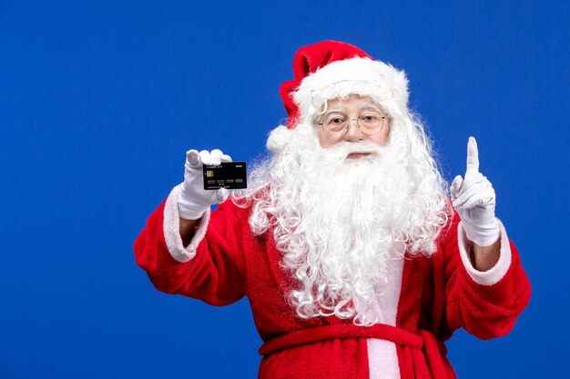 Вид спереди санта-клауса в красном костюме с черной банковской картой на синем подарочном рождественском празднике