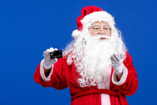 Front view santa claus in red suit holding black bank card on blue present xmas color holidays