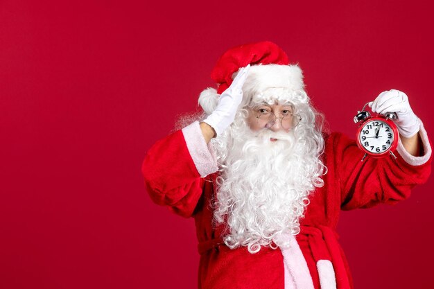 Front view santa claus in red suit holding clock on red xmas holiday emotion time