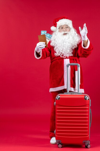 Front view of santa claus with bag holding tickets and preparing for trip on red wall