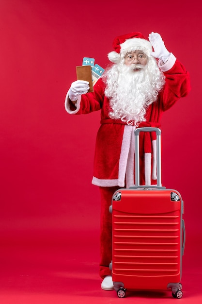 Front view of santa claus with bag holding tickets and preparing for trip on red wall