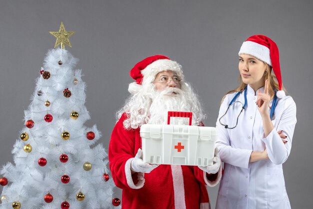 Front view of santa claus with female doctor who gave him first aid kit on the grey wall