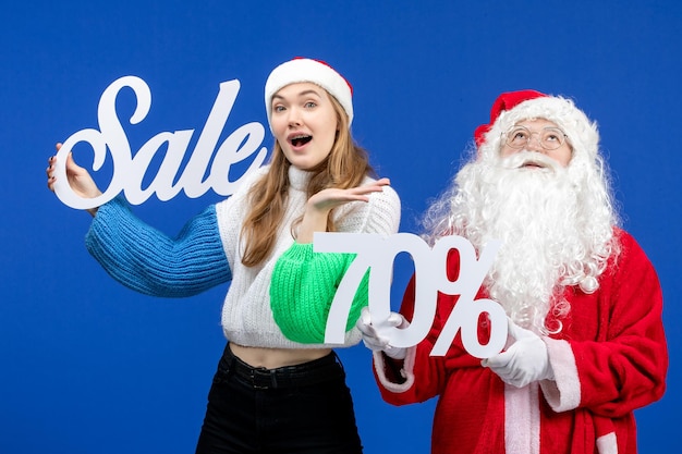 Free photo front view santa claus with female holding sale writings on blue holiday cold xmas new year snow shopping