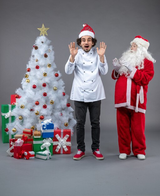 Front view of santa claus with male cook around christmas presents on grey wall