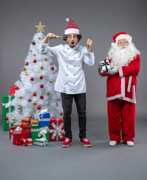 Front view of santa claus with male cook around christmas presents on grey wall