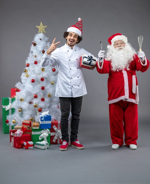 남성 요리사와 크리스마스 산타 클로스의 전면보기는 회색 벽에 주위에 선물