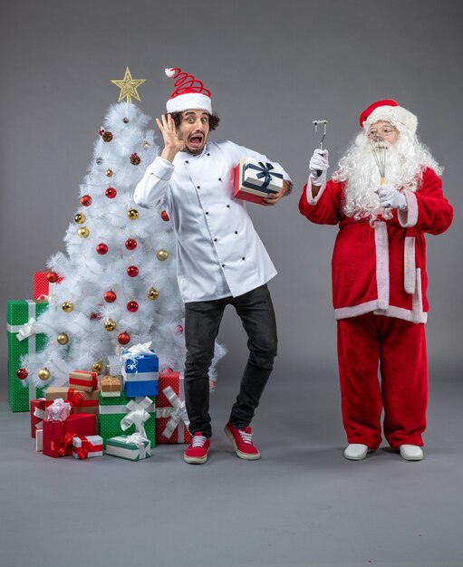 Front view of santa claus with male cook and christmas presents around on grey wall