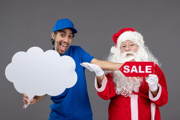 Front view of santa claus with male courier holding cloud sign and sale banner on grey wall